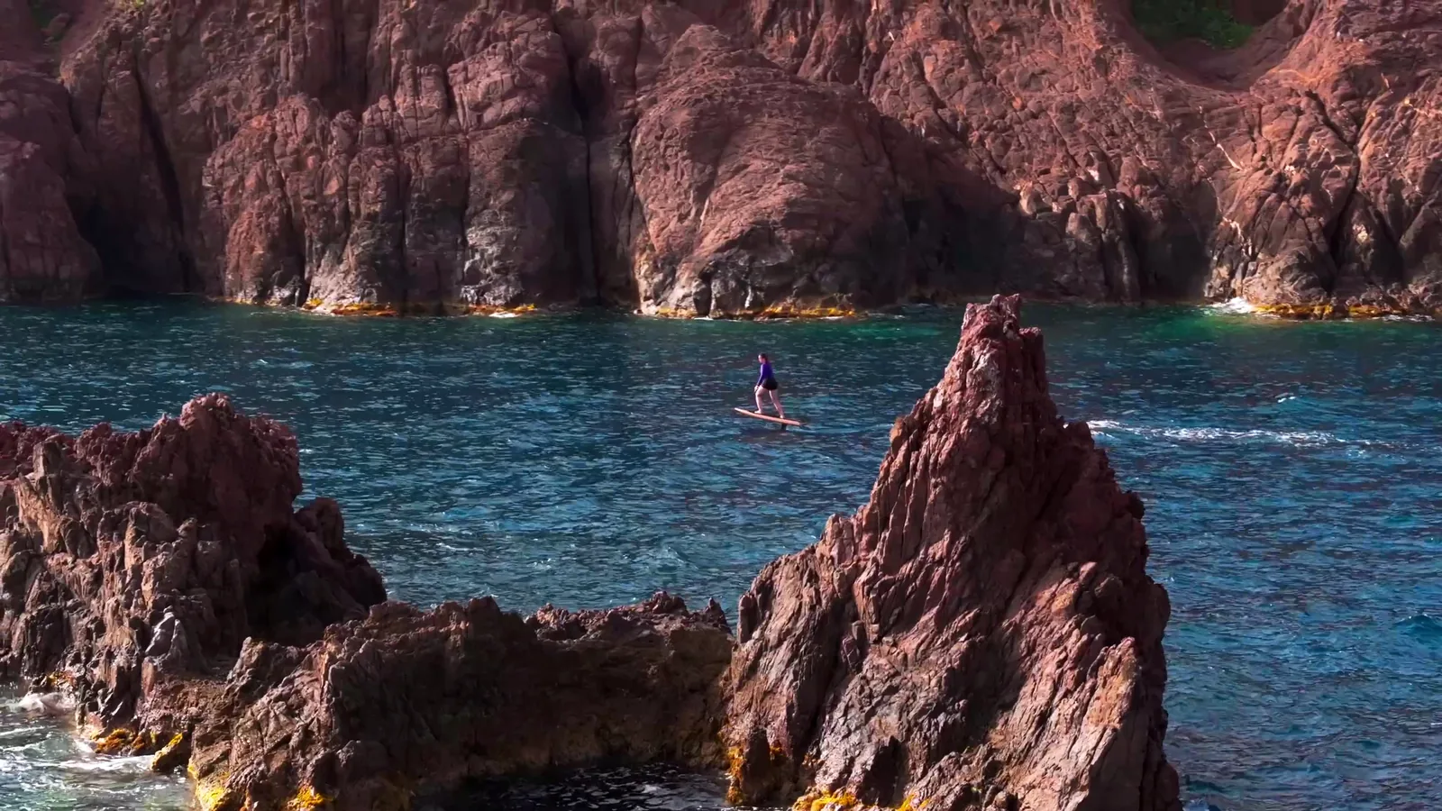 Vue aérienne : un rider glisse au-dessus d'une eau turquoise, sillage fin derrière l'aile.